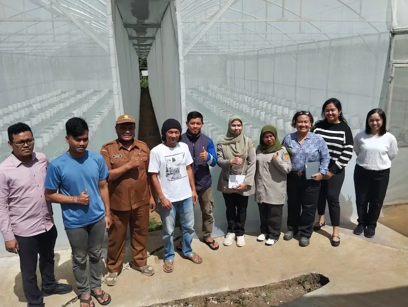 Farmers and community members standing in front of a greenhouse